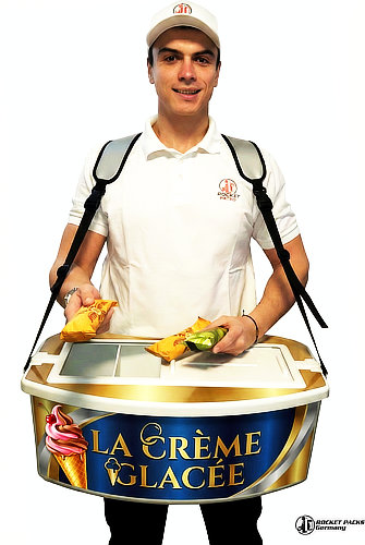 Vendeur ambulant avec un plateau isotherme vendant des glaces fraîches sur une plage bondée en été.